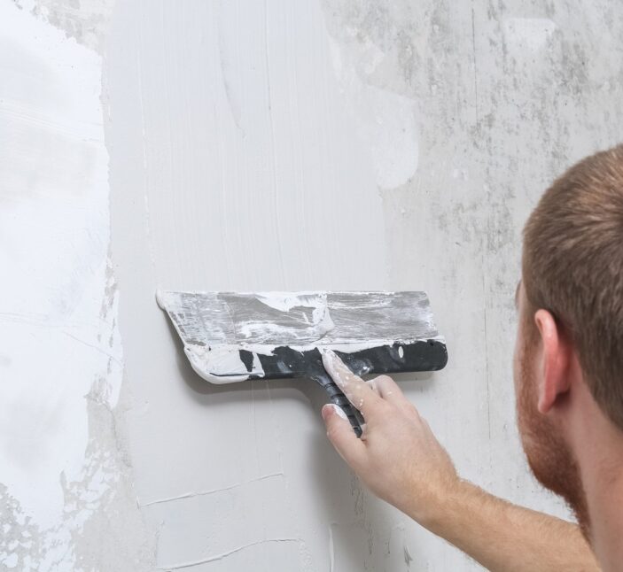 A male worker spreads the putty mixture and flattens the wall.